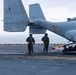 Two U.S. Marines in flight suits and helmets stand on the flight deck of a naval vessel beside a tiltrotor aircraft. The aircraft is marked with 'MARINES' and squadron designation 'VMM-' along with bureau number '168336' and tail code '04/8336'. The overcast sky and open ocean are visible in the background, indicating an at-sea operation.