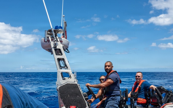 A U.S. Coast Guard rigid inflatable boat (RIB) is operating on open ocean under partly cloudy skies. Multiple personnel in Coast Guard uniforms and safety gear are visible, with some wearing helmets and orange vests. The image appears to capture an active maritime patrol or training operation.