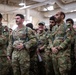 A group of military personnel from multiple nations are standing together in what appears to be a hangar or large indoor military facility. The group includes U.S. Army soldiers and personnel wearing Qatar Armed Forces uniforms, suggesting a joint military exercise or cooperative training event. The atmosphere appears relaxed and collegial, with some individuals smiling.