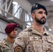 The image shows military personnel from multiple nations standing in formation inside what appears to be a hangar or large military facility. The foreground subject wears a Spanish military uniform with a black beret bearing a parachutist badge, identified by the name tape 'DELGADO' and an 'Ejército del Aire y del Espacio' patch. Behind him are US Army soldiers wearing maroon berets and MultiCam uniforms, one identified by the name tape 'GABAYAN'.