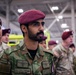 The image shows a group of military personnel wearing maroon berets in what appears to be an indoor military facility or hangar. The central figure is a soldier from the Qatar Armed Forces, identifiable by his name tape 'Bakhit Mohammed Saeed' and unit patch. Multiple nationalities appear to be represented, suggesting a joint military exercise or ceremony.