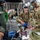 Military medical personnel in OCP (Operational Camouflage Pattern) uniforms are conducting aeromedical evacuation procedures aboard a large military transport aircraft, likely a C-17 Globemaster III. Two medics wearing aviation headsets are attending to patients on litters, using a bag-valve mask and monitoring equipment. The scene appears to be either a training exercise or an actual aeromedical evacuation mission, with numerous additional personnel seated in the background.