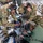 Military medical personnel in OCP (Operational Camouflage Pattern) uniforms are performing emergency medical care on a patient aboard what appears to be a military transport aircraft, likely a C-17 Globemaster. Three or more service members wearing communication headsets are actively treating the patient using a bag-valve mask for ventilation and medical monitoring equipment. This appears to be an aeromedical evacuation scenario, either a real operation or a training exercise.