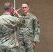 Two U.S. Air Force personnel in OCP (Operational Camouflage Pattern) uniforms are engaged in a formal military salute exchange, likely during a ceremony or official event. The individual facing the camera wears a 'U.S. Air Force' tape and what appears to be aviator wings on their uniform. The setting appears to be an indoor venue with wood-paneled walls, consistent with a conference room or event hall.