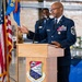 A senior U.S. Air Force enlisted member, identifiable by Chief Master Sergeant rank insignia, delivers a speech at a podium bearing the 934th Airlift Wing emblem. The ceremony appears to be a formal military event, likely a retirement or award ceremony, held inside an aircraft hangar. An American flag and a unit guidon are displayed to the left of the podium.