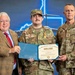 Three individuals pose for a formal military award ceremony photo. The central figure, wearing a U.S. Air Force uniform with the name tape 'WOLFE,' is holding a West Virginia National Guard certificate alongside a civilian in a tan blazer and a U.S. Army officer with the name tape 'SEWARD' bearing two-star general rank insignia. The certificate appears to be a West Virginia Distinguished Service Medal award.