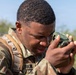 A U.S. Army soldier in MultiCam (OCP) camouflage uniform is closely examining a lensatic compass, likely taking a bearing or azimuth reading during a land navigation exercise. The soldier's name tape reads 'URKIN' (partially visible) and an American flag patch is visible on the left shoulder. The image appears to be taken outdoors in a training environment.