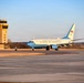 A United States of America government aircraft, appearing to be a C-40 or similar military transport, taxis on the runway at what is identified as Offutt Air Force Base (AFB). The aircraft features the distinctive white and powder blue livery associated with U.S. government/Air Force executive transport aircraft. The scene is captured during golden hour lighting with a tan control tower visible in the background.