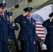 Four United States Air Force officers in dress blue uniforms are rendering a salute during a formal military ceremony. The event appears to be taking place at Joint Base San Antonio, as indicated by the partially visible banner in the background. The setting is likely a change of command or official military function held inside a hangar.