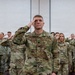 A large group of U.S. Air Force personnel in OCP (Operational Camouflage Pattern) uniforms are rendering a salute during what appears to be a formal military ceremony or formation. A central figure, prominently positioned in the foreground, displays a name tape reading 'JOHNSON' and a rank insignia consistent with a Lieutenant Colonel (oak leaf cluster), with 'U.S. AIR FORCE' tape visible on the chest. The setting appears to be an indoor venue such as a conference hall or event center.