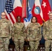 Four U.S. Army personnel in OCP (Operational Camouflage Pattern) uniforms pose for a formal group photograph in front of multiple flags including the U.S. flag, Japanese flag, and U.S. Army command flags. Name tapes visible on uniforms read Cheney, Lewis, Quintero, and Lancet from left to right. The setting appears to be an official U.S. Army Japan headquarters or command facility.