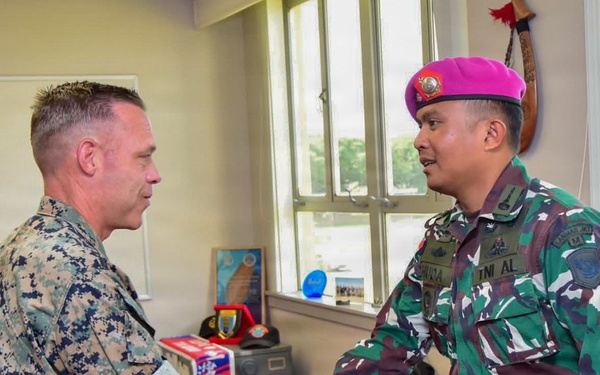 Two military personnel are shaking hands in what appears to be a military office setting. One individual wears US Marine Corps MARPAT digital camouflage, while the other wears Indonesian Armed Forces (TNI AL - Tentara Nasional Indonesia Angkatan Laut) camouflage uniform with a distinctive magenta/pink beret, indicating Indonesian Marine Corps (Korps Marinir). The meeting appears to be a formal bilateral military engagement or courtesy visit.