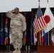A U.S. Army soldier in OCP (Operational Camouflage Pattern) uniform is rendering a salute during what appears to be a formal military ceremony. The soldier's name tape reads 'MELVIN' and the uniform displays 'U.S. ARMY' tape along with various patches. The setting includes a display of multiple flags including the American flag and the Japanese flag, suggesting a joint or international military event.