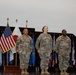 Three U.S. Army soldiers in OCP (Operational Camouflage Pattern) uniforms stand at attention on a stage during a formal military ceremony. They are positioned in front of a display of multiple flags including the U.S. flag and various state and territorial flags. Name tapes visible on the uniforms read 'CASUNDO,' 'DHALLION' (or similar), and 'MELVIN.'