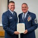 Two United States Air Force personnel pose together holding an official certificate or citation document. The individual on the right is a senior enlisted member displaying multiple service ribbons, a medal, and senior NCO rank insignia, suggesting this is an award or recognition ceremony. The officer on the left, identified by his name tag as 'WRIGHT,' appears to be presenting the award.