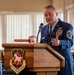 A senior U.S. Air Force enlisted member in dress blues is delivering a speech at a wooden podium bearing the insignia of the 467th Airlift Wing. The individual displays numerous service ribbons, medals, and what appears to be a Command Chief Master Sergeant rank insignia. The setting appears to be a formal military ceremony held in a dining facility or meeting hall.