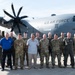 A group of approximately 13 individuals pose for a formal group photograph in front of a U.S. Air Force C-130J Super Hercules aircraft on a flight line or tarmac. The group consists of military personnel in various uniforms including flight suits, OCP (Operational Camouflage Pattern) uniforms, and one individual in civilian attire. The aircraft bears the tail number 1006 and 'U.S. AIR FORCE' markings.
