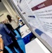 The image shows a medical or academic conference setting where researchers are gathered near a scientific poster presentation. The poster's 'Conclusions' section is prominently visible in the foreground, discussing menopause, hormone therapies, and provider coding. Several attendees are visible in the background engaged in discussion.