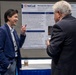 Two individuals are engaged in conversation at an academic or medical conference poster session. The poster behind them is from the National Intrepid Center of Excellence (NICoE) and concerns research on Perivascular Space in combat crewmen. One person appears to be presenting or explaining the research while the other listens.