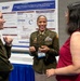 Three women are engaged in conversation at what appears to be a military medical research conference. The central figure is a U.S. Army officer in dress uniform presenting a research poster about 'Automated Clinical Decision Support for Triage and Monitoring of Military Casualties: A Modified Delphi Consensus Study' sponsored by the DHA (Defense Health Agency). The setting appears to be a professional academic or military medical symposium.