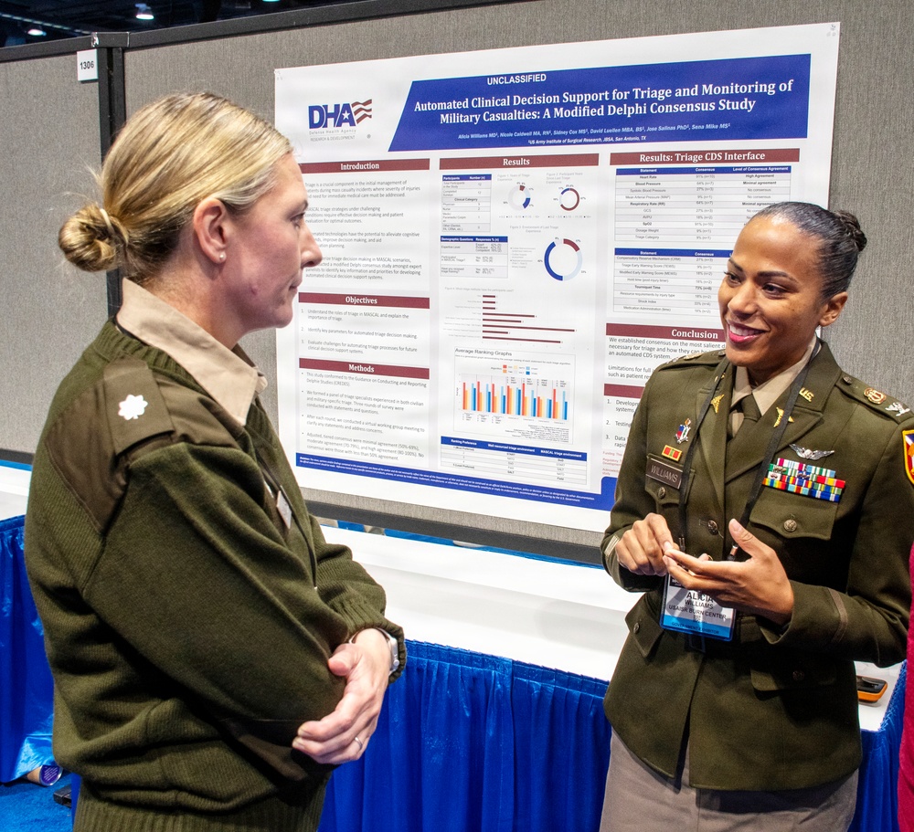 Two U.S. Army officers in dress green uniforms are engaged in conversation at what appears to be a military medical research conference or symposium. The officer on the right, identified by her name tag as 'Williams,' is presenting a research poster titled 'Automated Clinical Decision Support for Triage and Monitoring of Military Casualties: A Modified Delphi Consensus Study' sponsored by the Defense Health Agency (DHA). The poster displays research sections including Introduction, Methods, Results, and Conclusion with data visualizations.