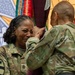 Two U.S. Army soldiers in MultiCam/OCP camouflage uniforms are participating in what appears to be a military ceremony, likely a change of command or change of responsibility. The soldier facing the camera, identified by the name tape 'BLAH' and wearing a Sergeant Major rank insignia, appears emotional while holding or receiving a unit guidon or flag. Military colors and flags are visible in the background.