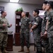 A U.S. Army soldier in OCP (Operational Camouflage Pattern) uniform is briefing or conversing with four military personnel wearing Republic of Korea (ROK) Army uniforms in what appears to be a military office. The setting includes a 'Blackhawks' unit insignia on the wall, suggesting this is a U.S. Army aviation unit headquarters. The interaction appears to be a formal military exchange or liaison visit.