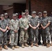 A group of approximately eleven military personnel pose for a formal group photograph in front of a brick building. The group includes both U.S. Army soldiers in OCP (Operational Camouflage Pattern) uniforms and Republic of Korea (ROK) Army soldiers in their distinctive digital camouflage uniforms with South Korean flag patches. This appears to be a joint military exchange or liaison visit between U.S. and South Korean armed forces.
