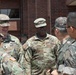 A group of military personnel in uniform are engaged in conversation outside a brick building. The group includes U.S. Army soldiers in OCP (Operational Camouflage Pattern) uniforms and what appear to be Republic of Korea (ROK) Army soldiers in their distinctive digital camouflage uniforms. The interaction appears to be a formal or semi-formal meeting between allied military forces.