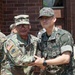 Two military personnel are posing together for a photo, shaking hands in a formal greeting. One is a U.S. Army soldier wearing OCP (Operational Camouflage Pattern) uniform with the name tape 'KOUNDET' and a Command Sergeant Major rank insignia, while the other wears a Republic of Korea (ROK) Army digital camouflage uniform with a two-star general rank insignia. The setting appears to be an outdoor area adjacent to a brick building, suggesting a bilateral military engagement or visit.