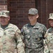 Three military personnel are posing together in front of a brick building. Two individuals wear U.S. Army OCP (Operational Camouflage Pattern) uniforms, while the center individual wears a Republic of Korea (ROK) Army digital camouflage uniform. The group appears to be participating in a joint military engagement or official visit.