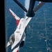 A United States Air Force Thunderbirds F-16 Fighting Falcon is captured during an aerial refueling operation with a tanker aircraft, viewed from above and behind the tanker's boom operator position. The jet displays the iconic red, white, and blue Thunderbirds livery with 'UNITED STATES AIR FORCE' lettering along the fuselage. A patchwork of agricultural fields is visible far below, suggesting the aircraft are at high altitude over a rural Midwestern landscape.