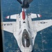 An aerial photograph taken from a tanker aircraft showing a U.S. Air Force Thunderbirds F-16 Fighting Falcon during an aerial refueling operation. The jet is viewed from directly above and behind, with the refueling boom visible at the top of the frame. The pilot is visible through the bubble canopy and appears to be giving a thumbs-up gesture.
