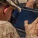A military personnel wearing desert camouflage (MARPAT pattern) uniform and cap is operating a Getac rugged tablet in an outdoor environment. The tablet displays 'TITAN-5V' on its screen and is connected via a cable. The setting appears to be an arid or semi-arid outdoor location.