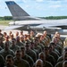 A large formation of military personnel in camouflage uniforms are assembled on an airfield tarmac in front of a U.S. Air Force F-16 Fighting Falcon jet. The aircraft's tail fin displays the word 'DULUTH' in blue lettering along with the serial number 'AF 414', indicating it belongs to the Duluth-based 148th Fighter Wing, Minnesota Air National Guard. The scene appears to be a formal military ceremony or group photo event.