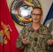 A U.S. Navy officer identified by name tape as 'HAWKINS' is speaking or briefing, gesturing with both hands. He is wearing the Navy Working Uniform (NWU Type III) with a single star insignia indicating the rank of Rear Admiral (Lower Half). He is positioned in front of a Naval Forces Atlantic emblem flanked by a U.S. Marine Corps flag and a U.S. Navy flag.