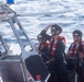 Four personnel wearing black helmets, sunglasses, and red life vests are aboard a rigid-hull inflatable boat (RHIB) on open water. The vessel is equipped with a Raymarine navigation/radar unit mounted on a metal frame, and a forward-mounted weapon or sensor barrel is visible. The letters 'USCG' are partially visible on the hull, identifying this as a United States Coast Guard vessel.