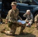 The image shows a group of military personnel, appearing to be Civil Air Patrol cadets and members, gathered outdoors near a vehicle. A central figure wearing OCP (Operational Camouflage Pattern) uniform with 'MASON' nametape and an Air Force tape is kneeling on one knee while holding documents or maps. Three other personnel are seated on the ground behind him, suggesting a briefing or training exercise is taking place.
