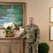 A U.S. Air Force service member in OCP (Operational Camouflage Pattern) uniform stands in what appears to be an upscale interior room, posing beside a wooden sideboard. The name tape reads 'BARNAS' and the branch tape reads 'U.S. AIR FORCE.' The setting appears to be a formal portrait or official photograph taken in a well-decorated residential or official quarters environment.