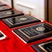 The image shows multiple military award plaques arranged on a red cloth-covered table. The plaques appear to be from the United States Marine Corps Combat Correspondents Association, featuring gold lettering and the Marine Corps seal on dark wood and black backgrounds. At least one plaque is legible enough to indicate a 'Visual Information and Excellence' award with 'First Place' designation.