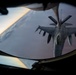 An aerial refueling operation is captured from the boom operator's window of a tanker aircraft, showing an F-16 Fighting Falcon receiving fuel via a refueling boom. The image is taken from below/behind the tanker looking down at the receiver aircraft against a twilight sky with cloud cover below. Text on the refueling boom reads 'KANSAS COYOTES', indicating a Kansas Air National Guard unit.