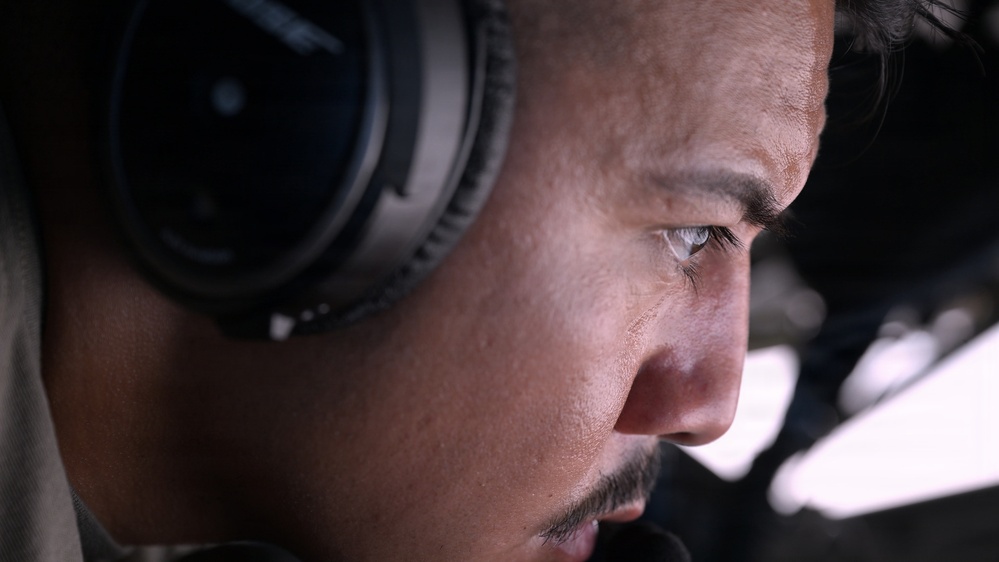 A close-up profile shot of a young man wearing over-ear headphones, gazing intently in a focused direction. The image is a tight facial crop emphasizing his eye, cheekbone, and jawline with shallow depth of field. The background is blurred, suggesting an indoor or enclosed environment.