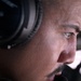 A close-up profile shot of a young man wearing over-ear headphones, gazing intently in a focused direction. The image is a tight facial crop emphasizing his eye, cheekbone, and jawline with shallow depth of field. The background is blurred, suggesting an indoor or enclosed environment.