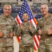 Three U.S. military personnel in OCP (Operational Camouflage Pattern) uniforms pose in front of an American flag inside what appears to be an indoor sports arena. The individuals are giving thumbs-up gestures and smiling. Name tapes and branch insignia are visible on their uniforms, identifying two as U.S. Army and one as U.S. Air Force.