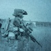The image shows two heavily equipped soldiers in full combat gear standing in an open field with tall grass. The photo has a distinctive blue-tinted, grainy quality consistent with night-vision device photography or a thermal/NVG-filtered camera. The soldiers appear to be on patrol or conducting a tactical movement.