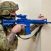 A U.S. Air Force staff sergeant named Taboada is conducting a tactical training exercise indoors, holding a blue training rifle (inert/simunition weapon used for drills). The soldier is in full multicam combat gear including a tactical helmet, face covering, and plate carrier, and is positioned against a wall in a shooting stance. The blue-colored weapon indicates this is a non-lethal training aid used in force-on-force or active shooter response exercises.