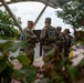 A group of National Guard soldiers in camouflage uniforms are gathered near the Eastern Market Metro station in Washington, D.C. At least three to four personnel are visible, with one soldier's vest clearly labeled 'NATIONAL GUARD' on the back. The scene appears to be a routine assembly or briefing near a public transit entrance.