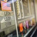 A military shadow box or display case containing U.S. Army memorabilia belonging to a service member with the surname 'LEON'. The display includes multiple name tapes in different camouflage patterns, a U.S. flag patch, and various military insignia and ribbons. The items represent a collection of uniform elements and service memorabilia typical of a military career display.