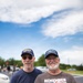 Two older men stand together in a parking lot, both wearing U.S. Navy submarine-related caps and apparel. The man on the right wears a shirt reading 'Remember Submarine Veterans' and 'USS GATO SSN-615 Permit-Class Nuclear-Powered Attack Submarine.' Both appear to be submarine veterans or enthusiasts attending a commemorative or community event.