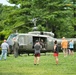 A military UH-1 'Huey' helicopter, marked with the number '170' and 'UNITED' (States Army) on its fuselage, is displayed on a grassy field surrounded by civilian visitors. The scene appears to be a public airshow, military heritage event, or museum display where attendees are viewing and photographing the aircraft up close. Several people are gathered around the open cabin of the helicopter, with some appearing to sit inside or inspect the interior.